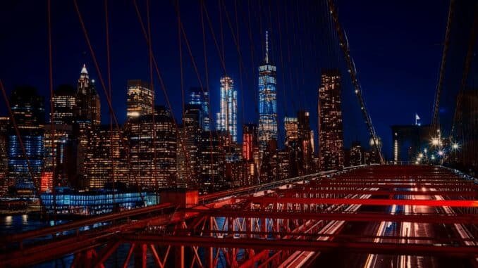 A breathtaking night view featuring the New York City skyline and iconic Brooklyn Bridge illuminated in vibrant colors.