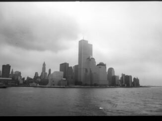Grayscale view of New York City skyline featuring the Twin Towers across the harbor.