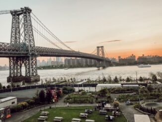 View of Williamsburg Bridge spanning East River at sunset with New York City skyline background.