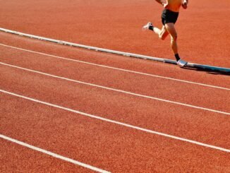 Athlete running on a red track in an outdoor stadium on a sunny day.
