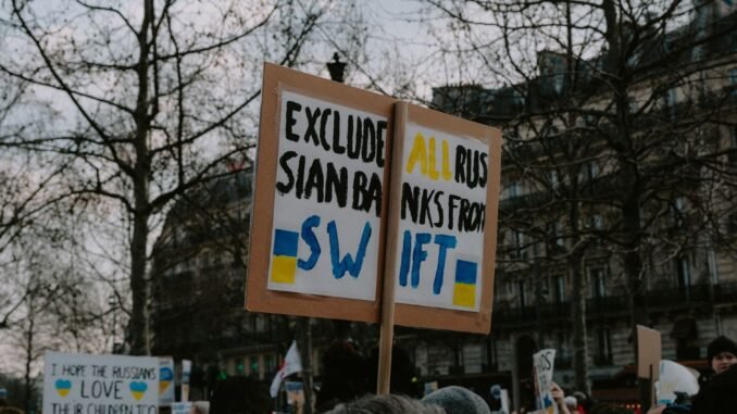Crowd gathered with placards during a protest against Russian banks in an urban setting.