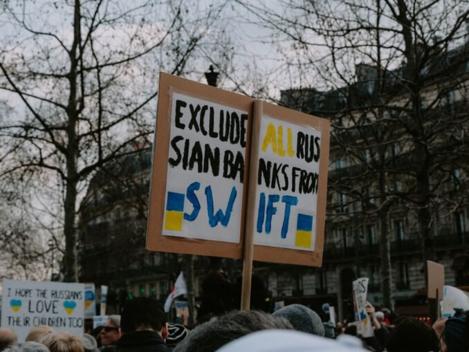 Crowd gathered with placards during a protest against Russian banks in an urban setting.