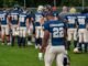 Football team players in helmets and uniforms preparing on the field.