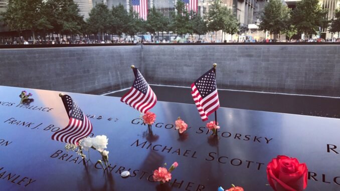 A poignant tribute at the 9/11 Memorial in NYC with flags and flowers honoring victims.