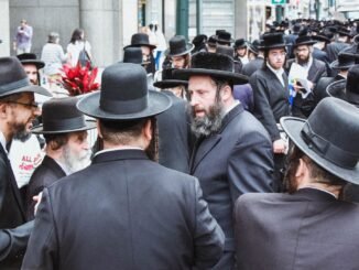 Group of Orthodox Jewish men gathered on a busy street in New York City.