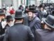 Group of Orthodox Jewish men gathered on a busy street in New York City.