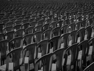 Black and white image of rows of empty plastic chairs creating a pattern.