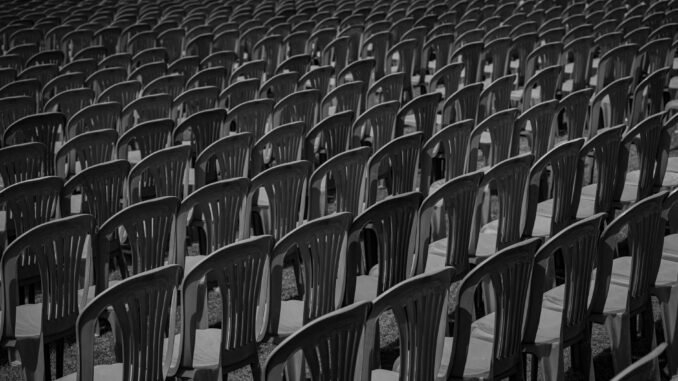 Black and white image of rows of empty plastic chairs creating a pattern.