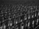 Black and white image of rows of empty plastic chairs creating a pattern.