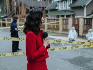 Female journalist reporting live on a crime scene investigation with police presence outdoors.