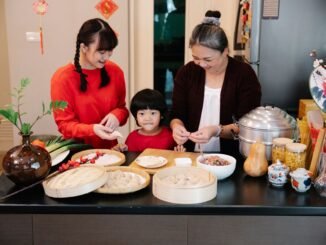 Cheerful Asian grandma with boy and female teen preparing dumplings at table with minced beef filling at home