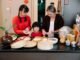 Cheerful Asian grandma with boy and female teen preparing dumplings at table with minced beef filling at home