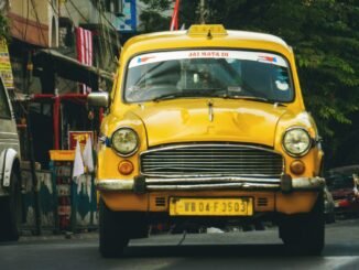 Classic yellow taxi driving through the vibrant streets of Kolkata, India.