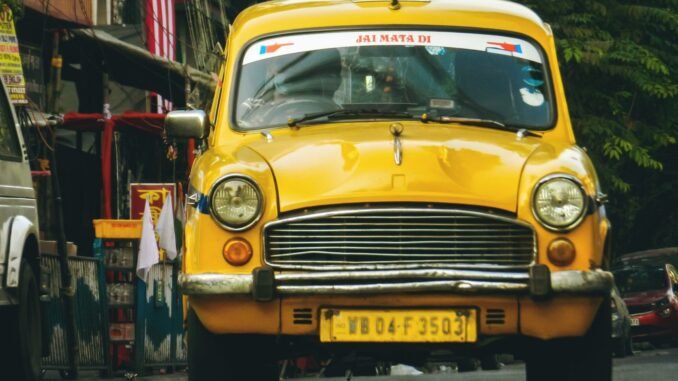 Classic yellow taxi driving through the vibrant streets of Kolkata, India.
