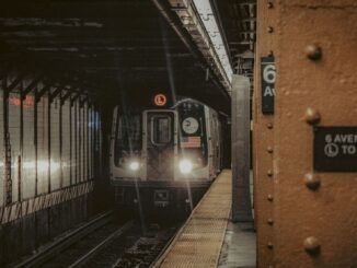 A New York City subway train approaching the platform at 6th Avenue station at night.