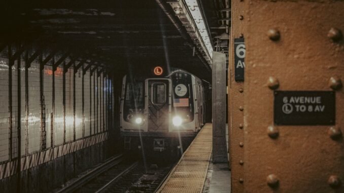 A New York City subway train approaching the platform at 6th Avenue station at night.