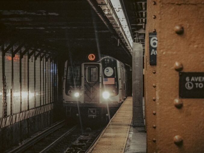 A New York City subway train approaching the platform at 6th Avenue station at night.